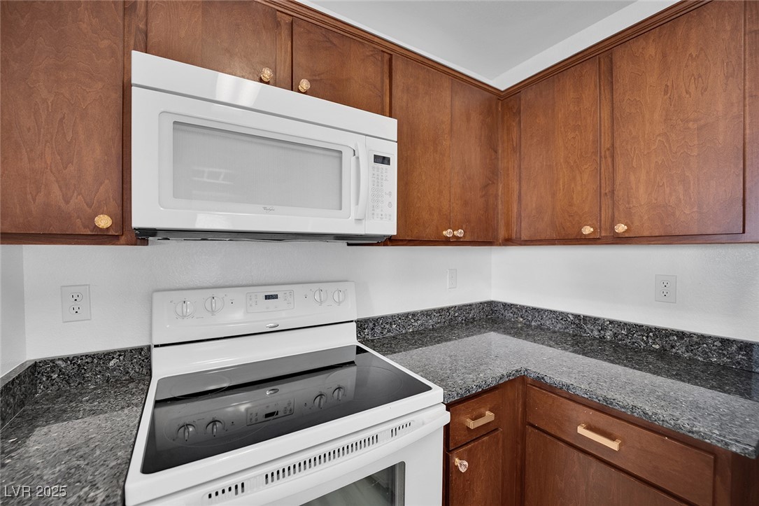 2300 East Silverado Ranch Boulevard, Unit 1189 Las Vegas, NV 89123 - Photo 16 of 27 Kitchen with white appliances, brown cabinets, and dark stone counters