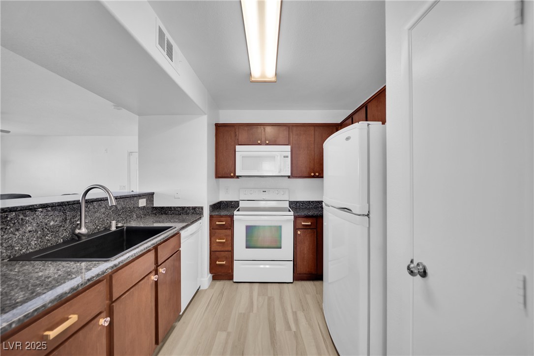 2300 East Silverado Ranch Boulevard, Unit 1189 Las Vegas, NV 89123 - Photo 17 of 27 Kitchen featuring white appliances, light wood-type flooring, dark stone counters, and brown cabinets