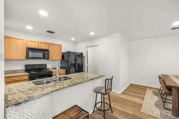 a kitchen with stainless steel appliances granite countertop a stove a sink a refrigerator white cabinets and wooden floor