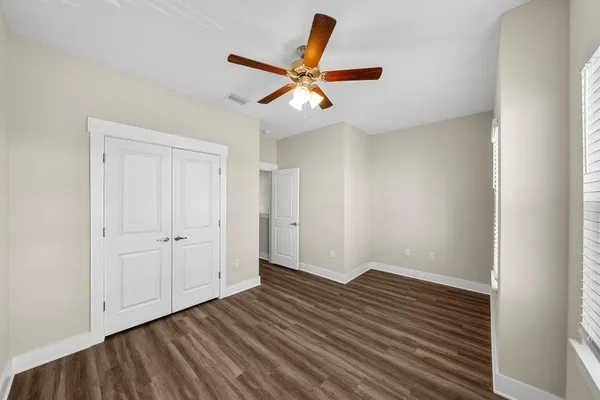 an empty room with wooden floor ceiling fan and window