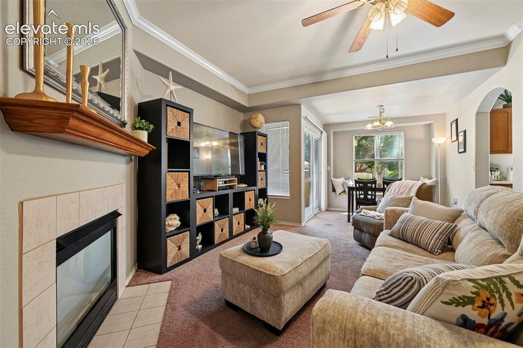 3715 Riviera Grove, Unit 101 Colorado Springs, CO 80922 - Photo 11 of 36 Living area featuring a fireplace with a tile surround and wood mantle, a ceiling fan, and carpet flooring