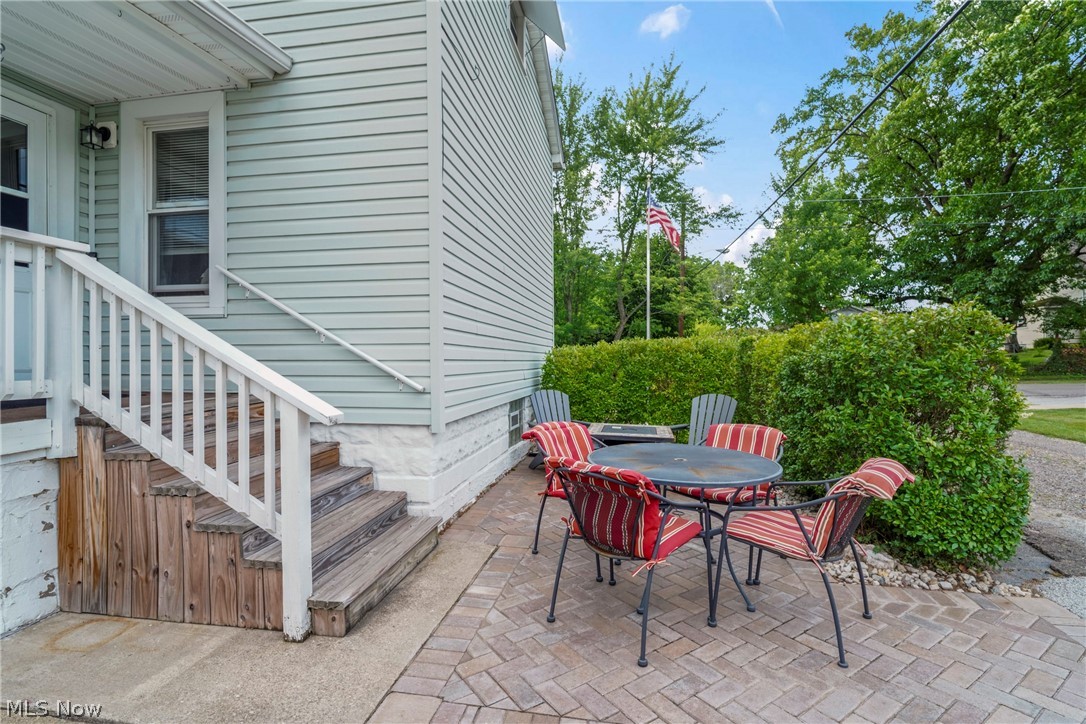 629 Clinton Street Niles, OH 44446 - Photo 29 of 50 Paved patio area featuring brick-patterned pavers, mature perimeter hedges, and an external wooden staircase with a white railing