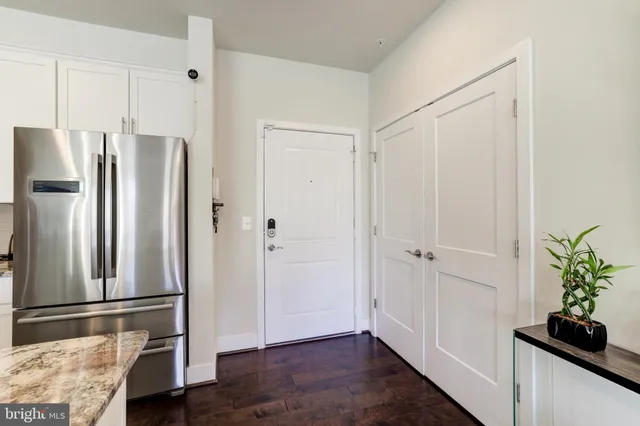 a view of a refrigerator in kitchen and an empty room with wooden floor