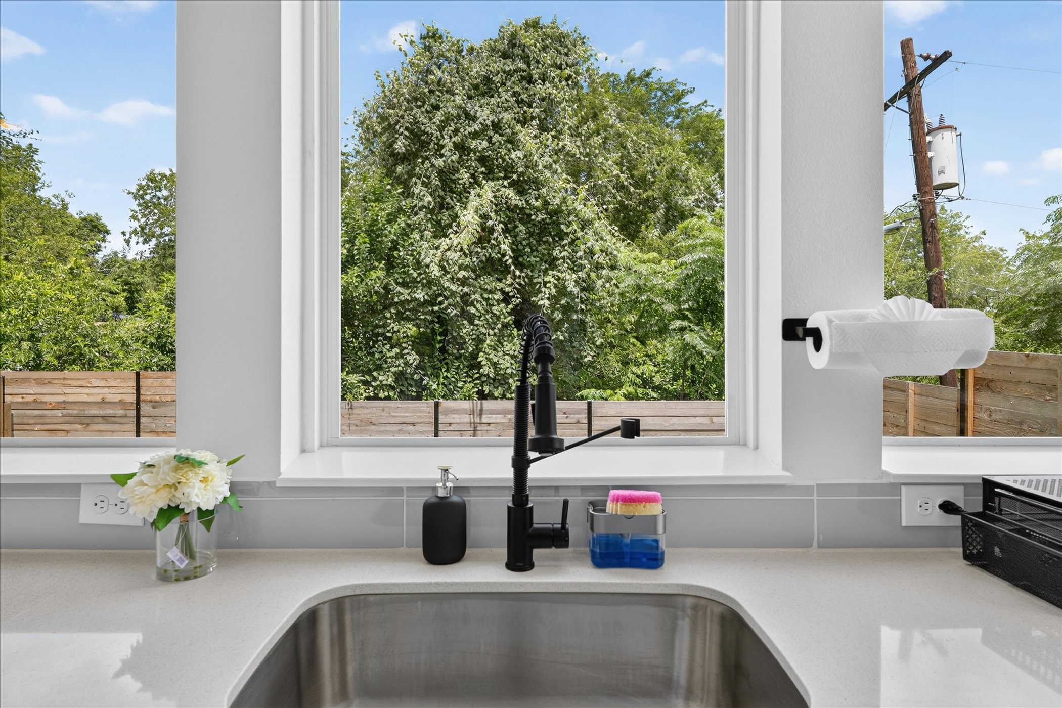 2000 Riverside Farms Road, Unit 8101 Austin, TX 78741 - Photo 10 of 41 Bright, modern kitchen sink area with a large window offering a lush green view. Features a sleek black faucet, white countertops, and convenient under-cabinet outlets.