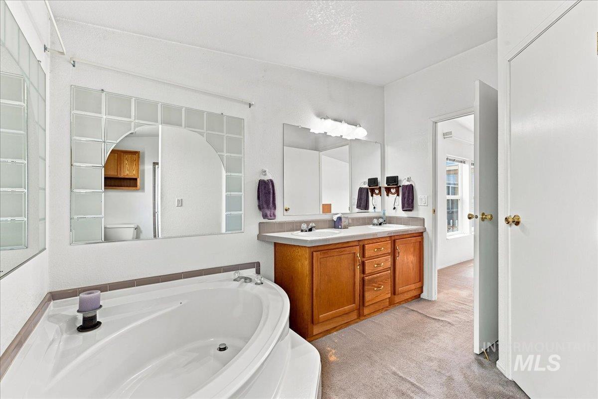 310 Frontage Road Grand View, ID 83624 - Photo 20 of 38 Bathroom featuring a corner soaking tub with deck, dual vanity with wood cabinetry, and a large mirror with integrated glass block accents