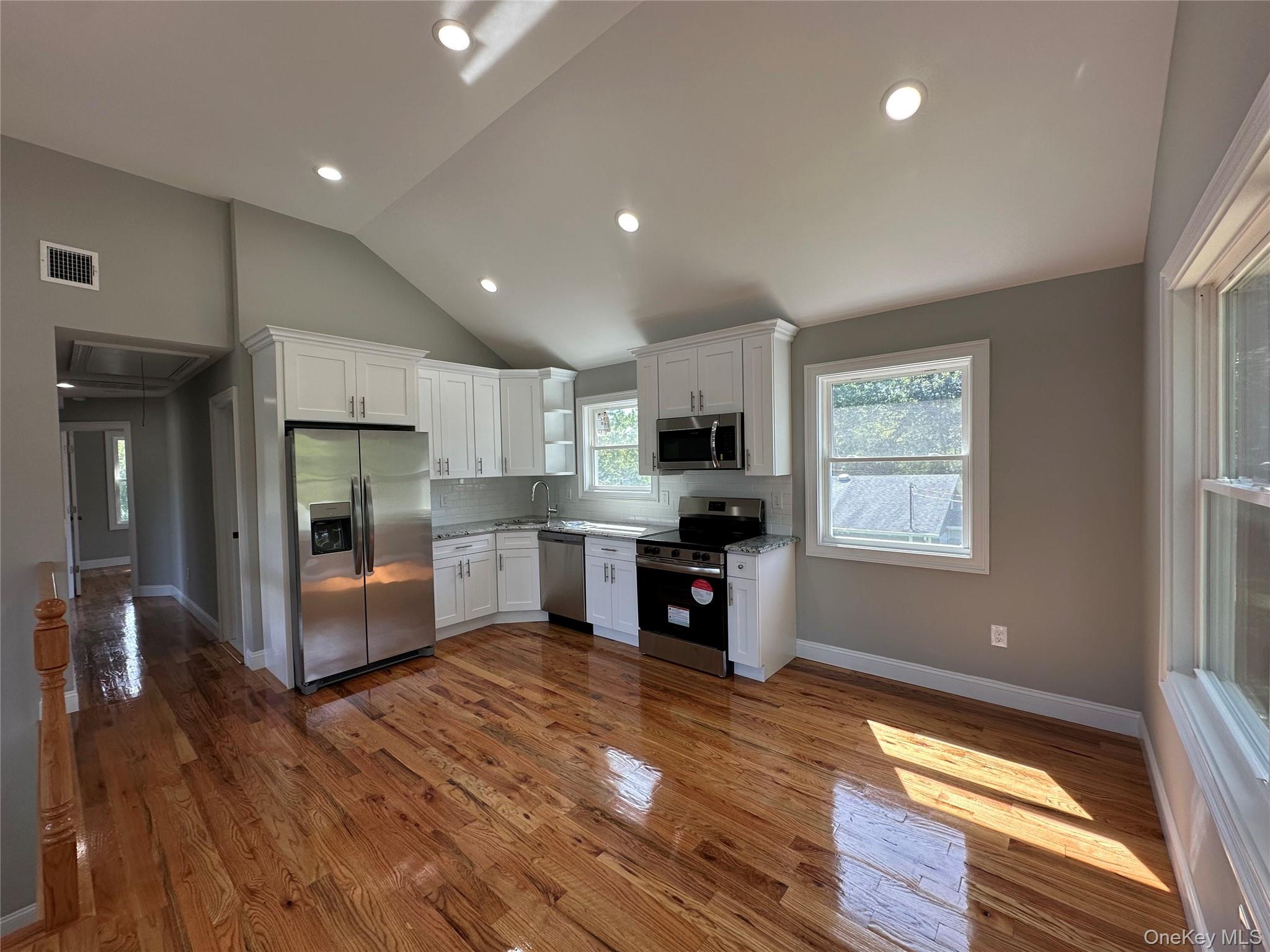 214 Forest Road West Mastic Beach, NY 11951 - Photo 2 of 24 Open-concept kitchen and living area featuring wood-finish flooring, white cabinetry, stainless steel appliances, and recessed lighting