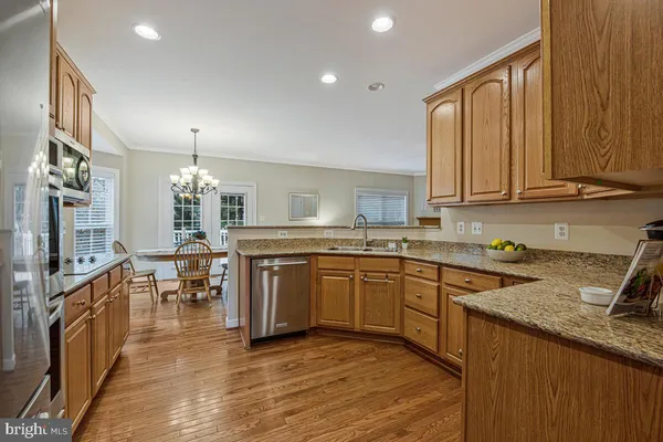 a kitchen with stainless steel appliances granite countertop a stove top oven a sink dishwasher a dining table and chairs with wooden floor