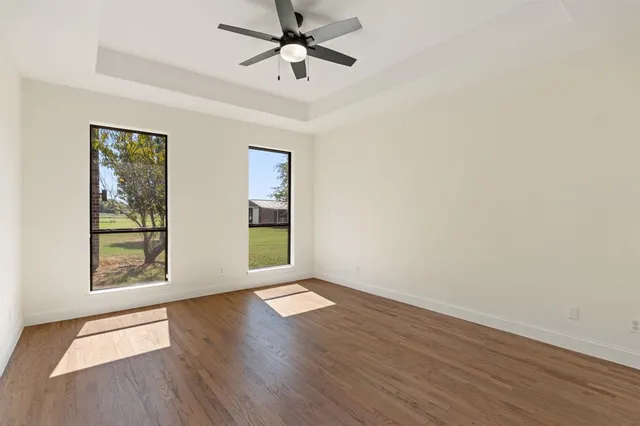an empty room with wooden floor chandelier fan and windows