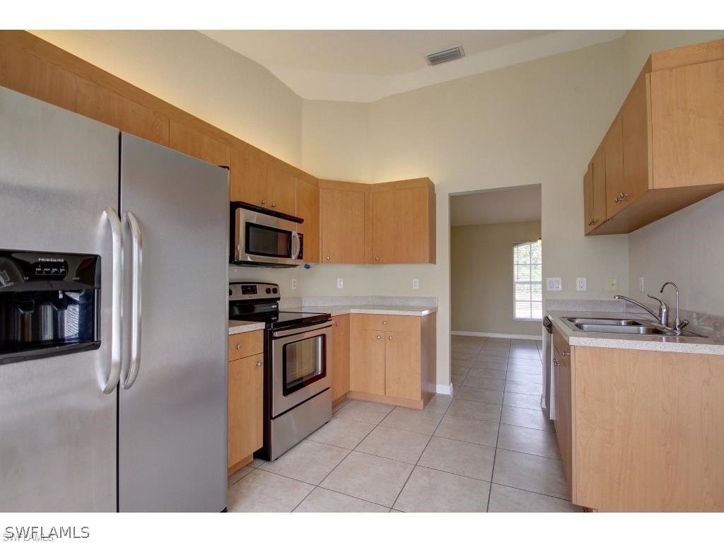 101 West 12th Street Lehigh Acres, FL 33972 - Photo 3 of 7 a kitchen with stainless steel appliances granite countertop a refrigerator a stove and a sink with wooden cabinets
