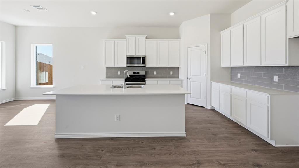 4163 Waldron Trail Forney, TX 75126 - Photo 2 of 30 Open-concept kitchen featuring an island with an undermount sink, stainless steel appliances, white cabinetry, a subway tile backsplash, and wood-finish flooring