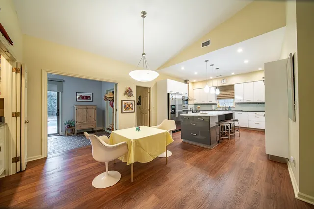 a open kitchen with stainless steel appliances granite countertop a refrigerator a stove top oven a dining table and chairs with wooden floor