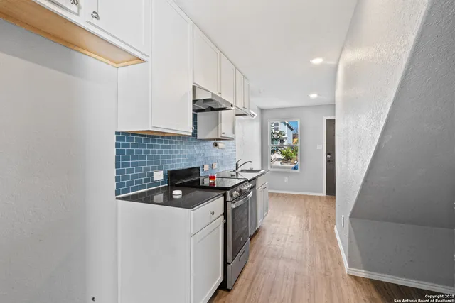 a kitchen with granite countertop a sink a stove top oven a counter space and cabinets