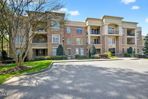a front view of a residential apartment building with yard and parking
