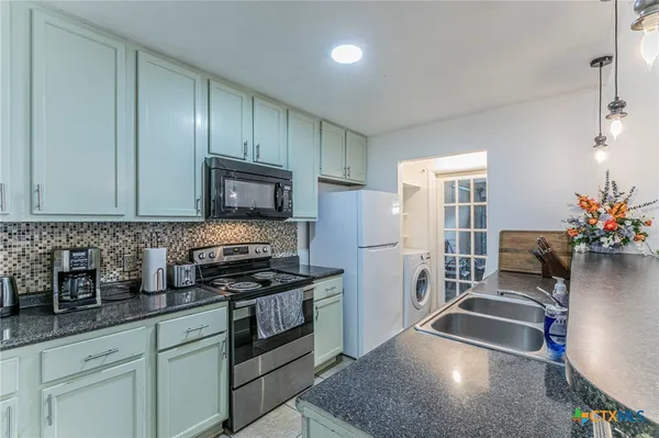 a kitchen with granite countertop a stove a sink and a refrigerator