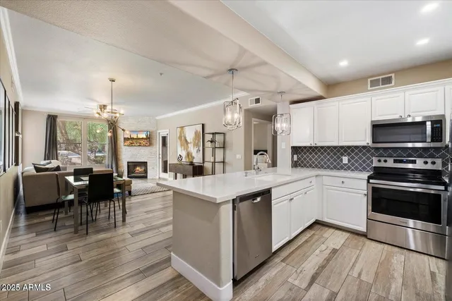 a open kitchen with stainless steel appliances granite countertop a stove top oven a sink dishwasher a dining table and chairs with wooden floor