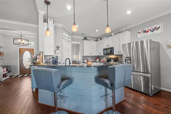 a kitchen with stainless steel appliances granite countertop a refrigerator a sink dishwasher a dining table and chairs with wooden floor