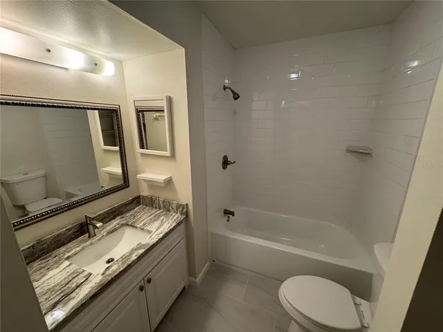 a bathroom with a granite countertop bathtub shower sink vanity and toilet