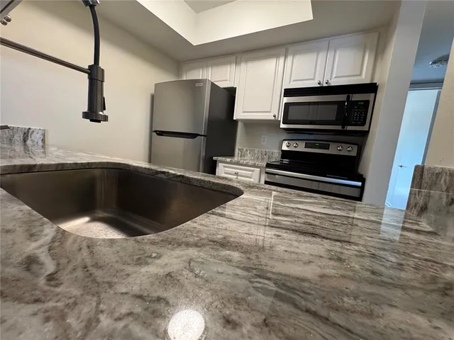 a kitchen with stainless steel appliances kitchen island granite countertop a sink and a refrigerator