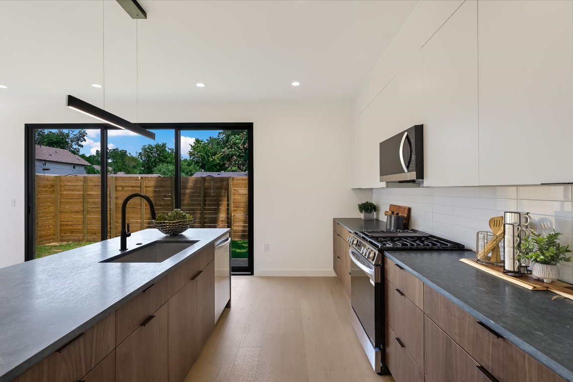 2705 Francisco Street, Unit A Austin, TX 78702 - Photo 6 of 21 Kitchen with modern cabinets, appliances with stainless steel finishes, light wood finished floors, dark countertops, and decorative backsplash