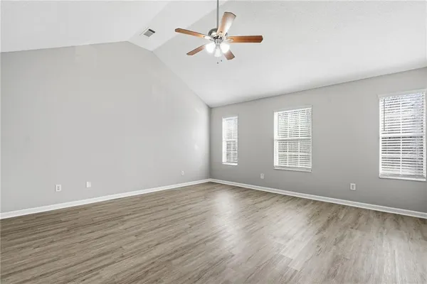 an empty room with wooden floor chandelier fan and windows