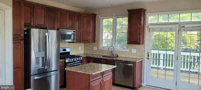 a kitchen with stainless steel appliances granite countertop a refrigerator a sink a stove a washer and dryer with wooden floor