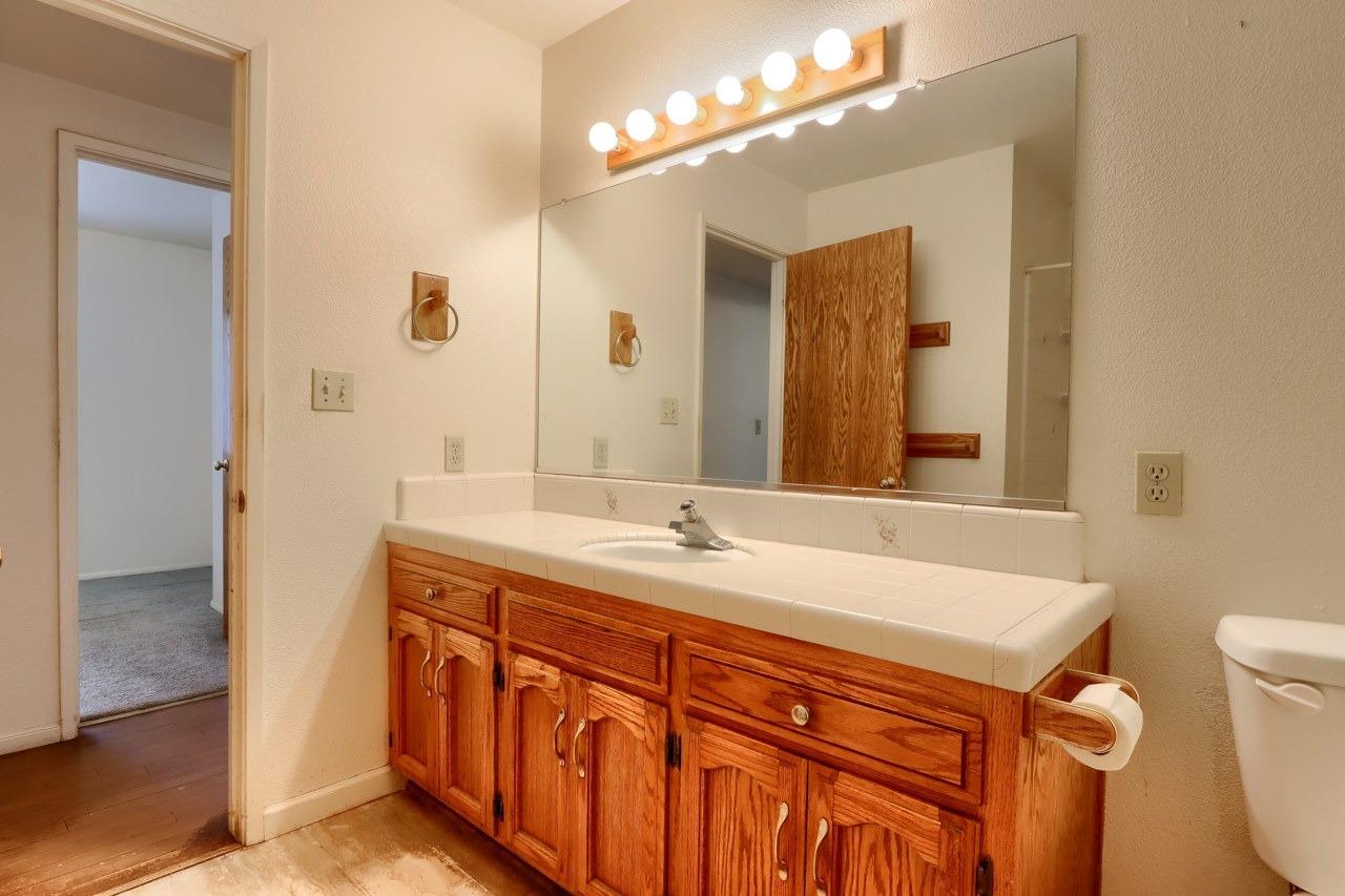 51973 Montgomery Drive Oakhurst, CA 93644 - Photo 27 of 50 a bathroom with a granite countertop sink a toilet a mirror and shower