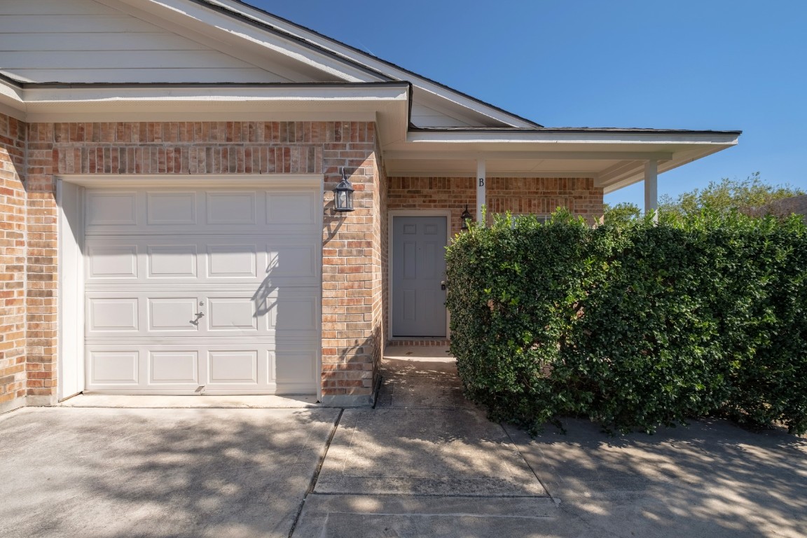 View of exterior entry featuring brick siding, covered porch, driveway, and a garage