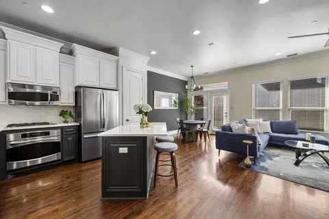 a kitchen with stainless steel appliances granite countertop a refrigerator a stove top oven a dining table and chairs with wooden floor