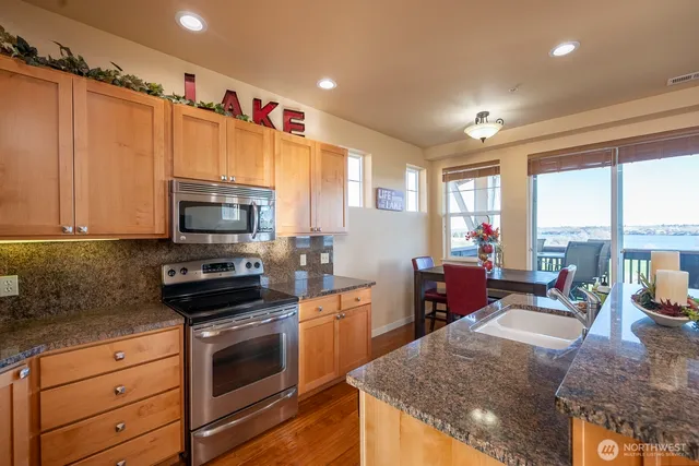 a kitchen with stainless steel appliances kitchen island granite countertop a stove a sink dishwasher and a microwave with wooden floor