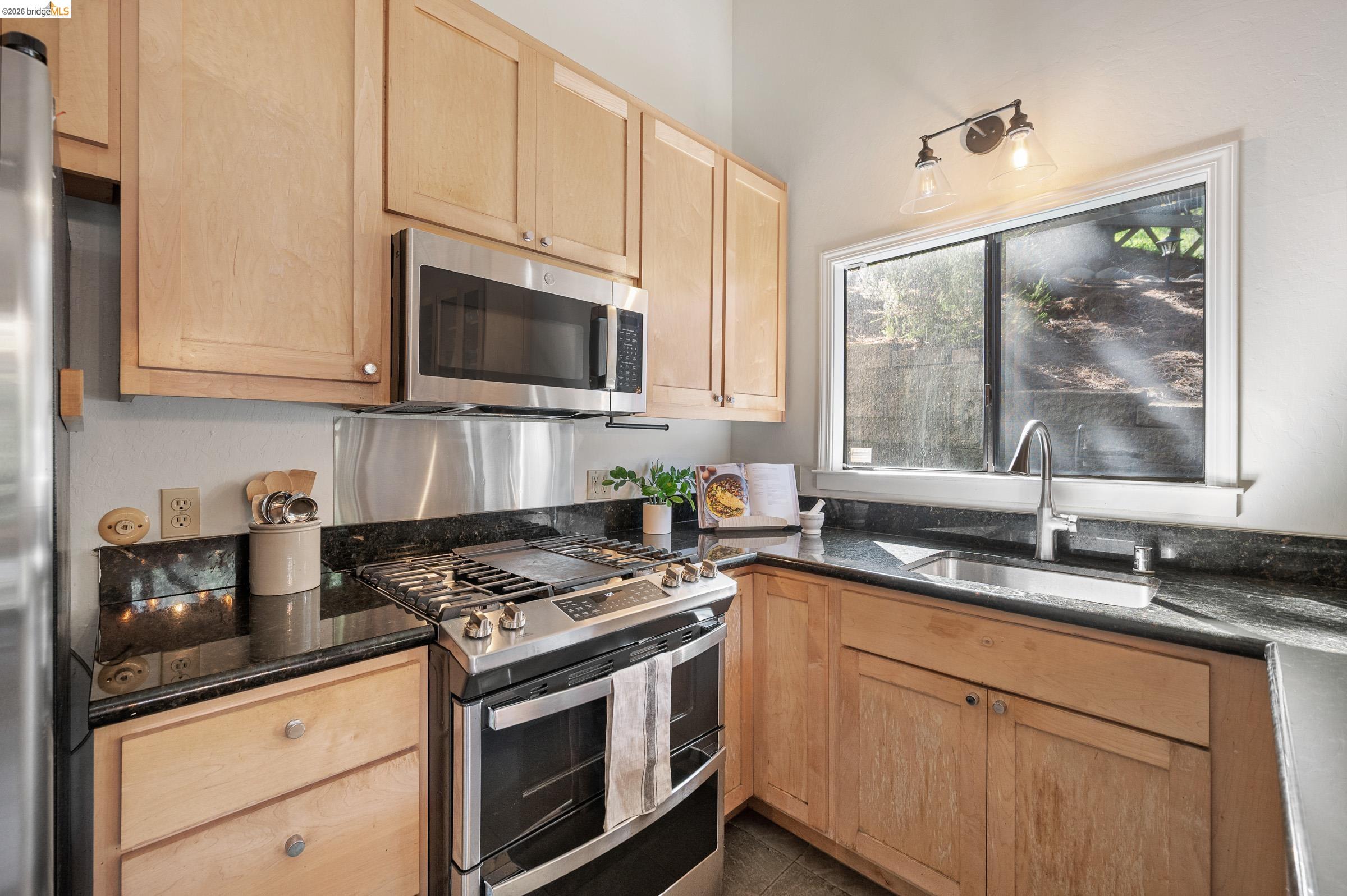 6600 Heather Ridge Way Oakland, CA 94611 - Photo 23 of 66 Kitchen featuring natural wood cabinetry, dark granite countertops, stainless steel appliances, a gas range, and an undermount sink