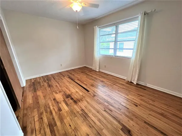 an empty room with wooden floor fan and windows