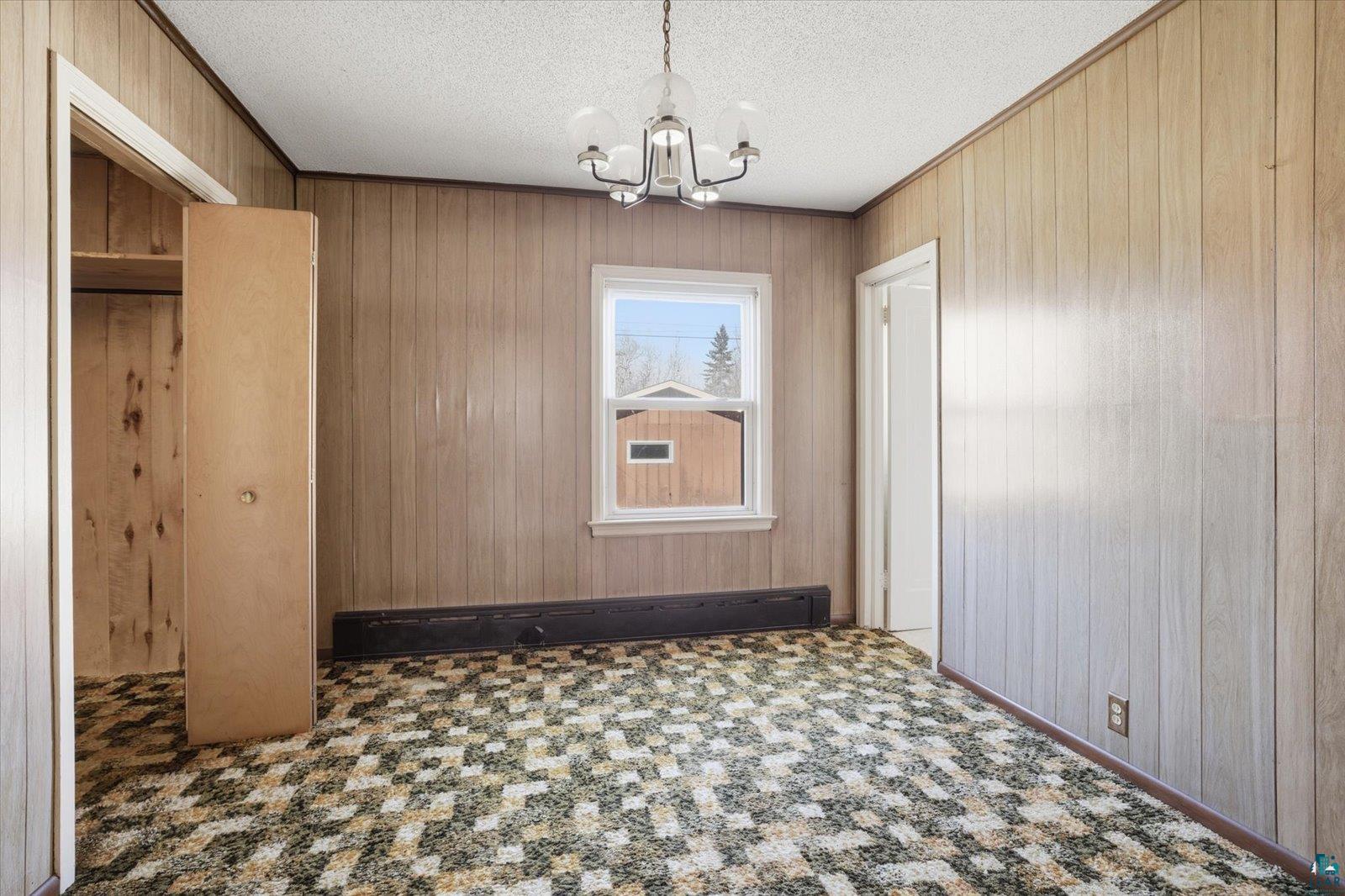 709 Michigan Street Hibbing, MN 55746 - Photo 13 of 47 Unfurnished dining area with hanging lights, ornamental molding, a textured ceiling, and wooden walls