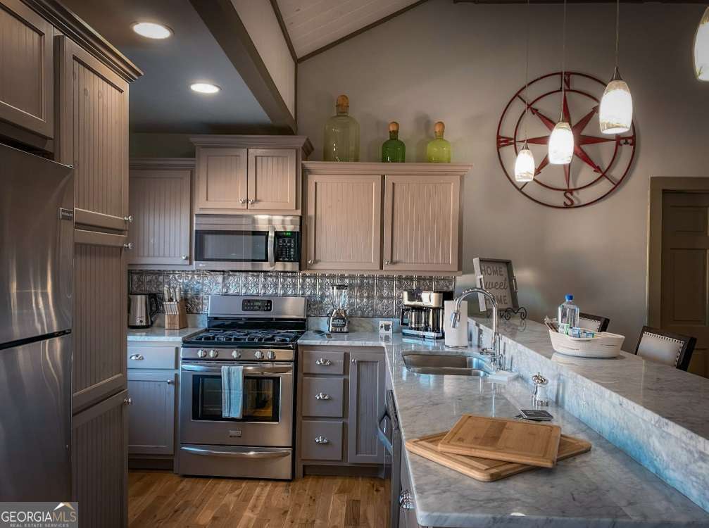 a kitchen with stainless steel appliances granite countertop a stove a sink dishwasher and a refrigerator with wooden floor