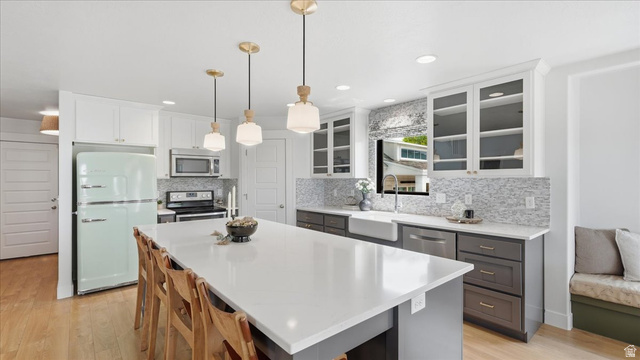 2038 East Ranch Road Eagle Mountain, UT 84005 - Photo 12 of 66 Kitchen featuring an expansive center island with seating, white shaker-style upper cabinetry, dark lower cabinetry, a farmhouse sink, and a patterned tile backsplash