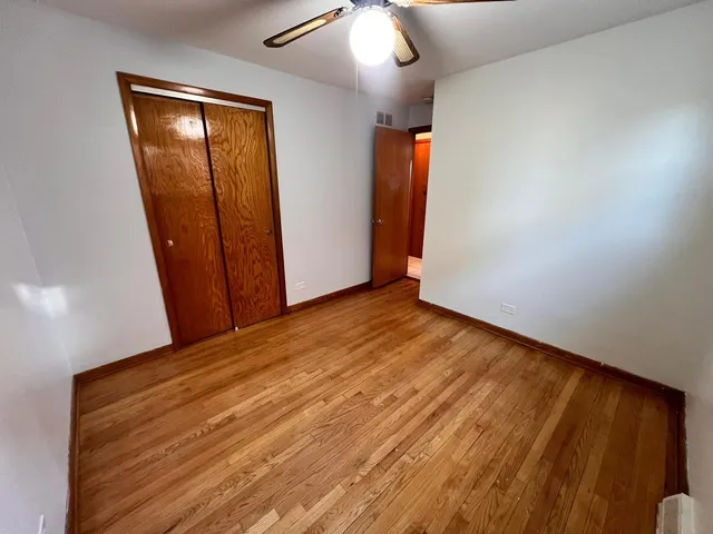 an empty room with wooden floor and way to kitchen