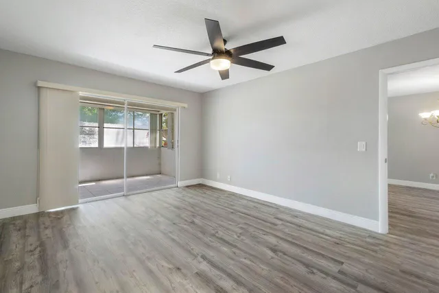 a view of an empty room with wooden floor and a ceiling fan