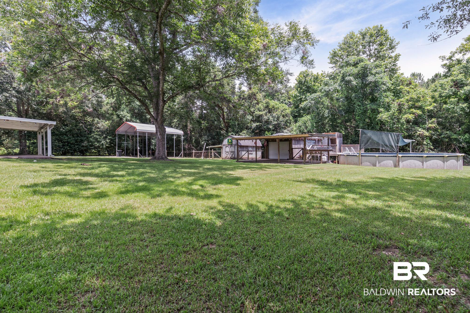 6933 Burbank Court Mobile, AL 36619 - Photo 23 of 25 Expansive green lawn with mature trees, an above-ground pool, and multiple covered structures