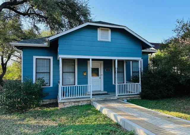 a view of brick house with a yard plants and large tree
