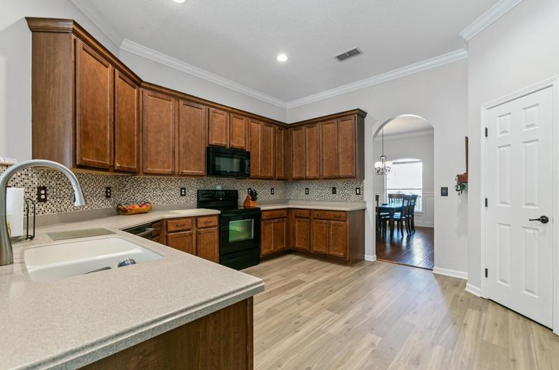 2724 North Portofino Road St. Augustine, FL 32092 - Photo 36 of 86 Kitchen with arched walkways, black appliances, light wood-style flooring, crown molding, and tasteful backsplash