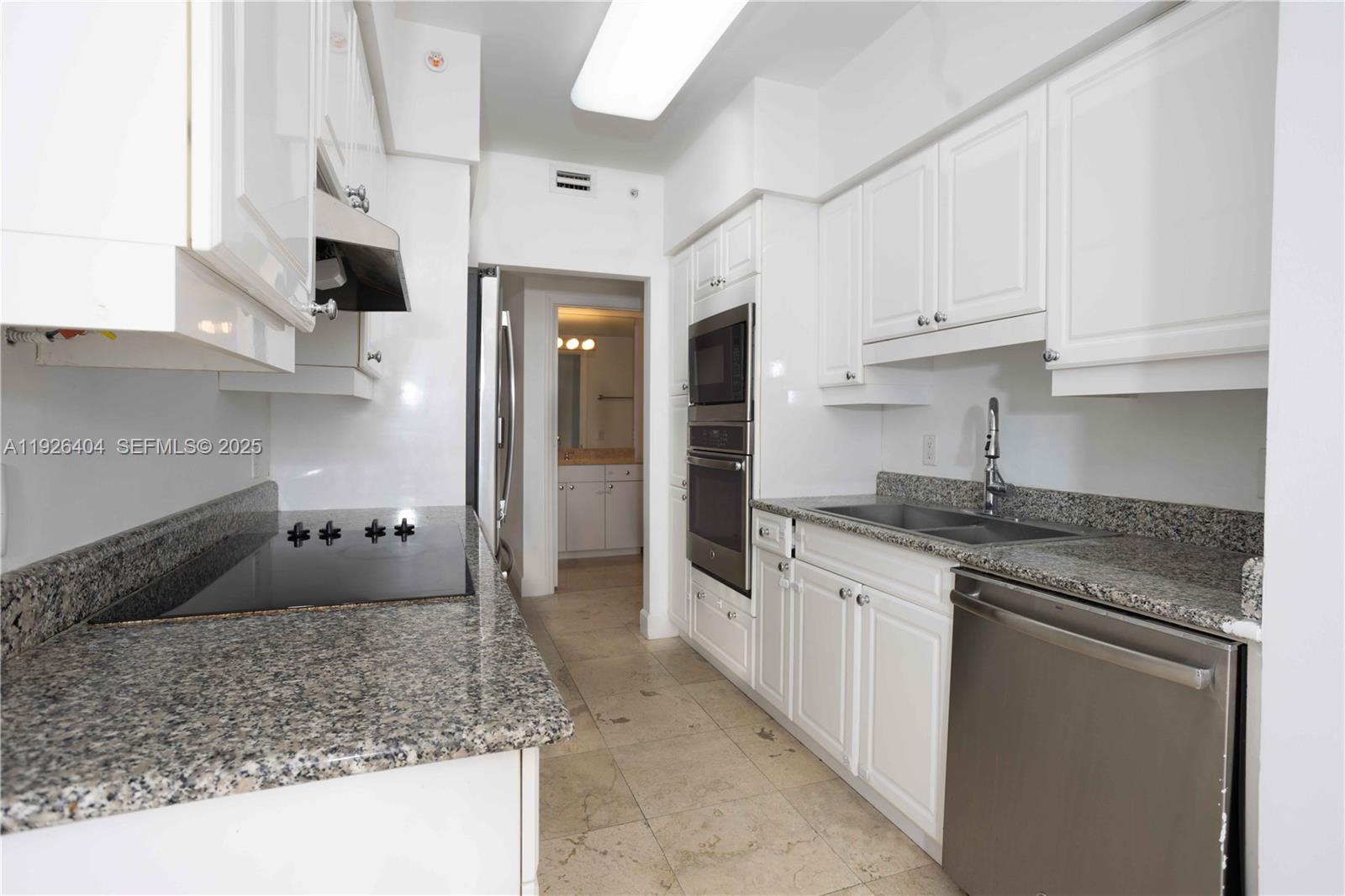 4779 Collins Avenue, Unit 504 Miami Beach, FL 33140 - Photo 9 of 45 a kitchen with granite countertop a sink and white cabinets