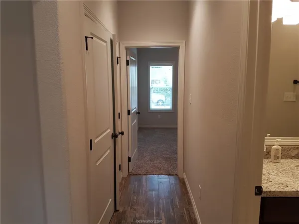 a view of a hallway with wooden floor and a bathroom