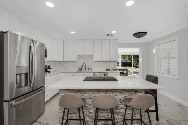 a kitchen with granite countertop a refrigerator a stove a sink and chairs