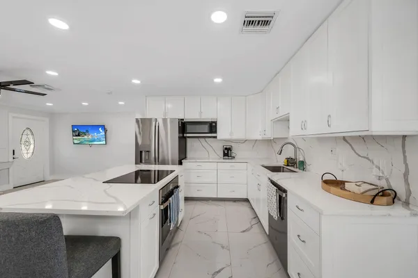 a kitchen that has a lot of white cabinets and stainless steel appliances