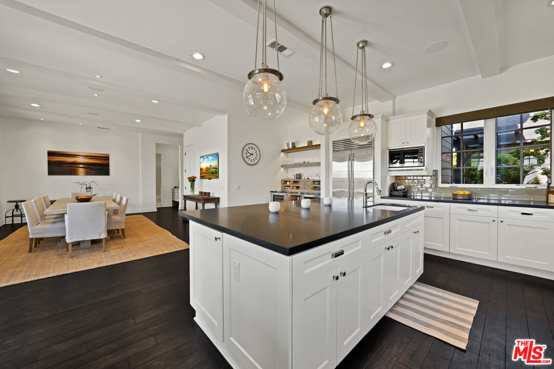28850 Hampton Place Malibu, CA 90265 - Photo 13 of 58 a large white kitchen with a large island oven a sink dishwasher and a dining table with wooden floor