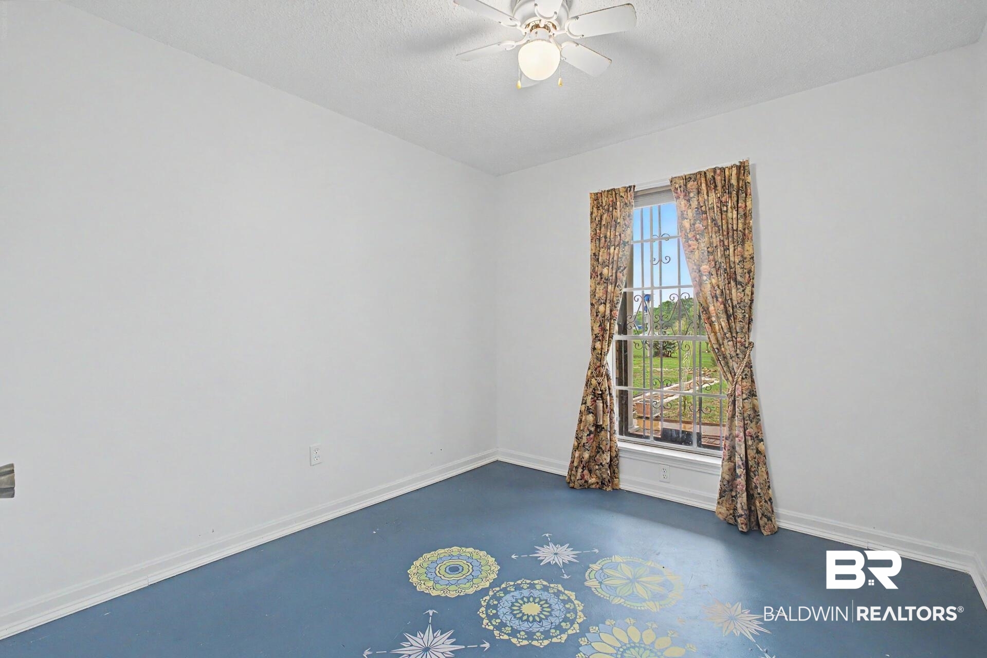 3791 Robinsonville Road Atmore, AL 36502 - Photo 36 of 47 Room featuring a ceiling fan, a window with security bars, painted blue flooring with decorative medallions, white baseboards, and white walls