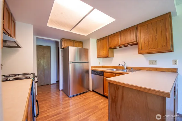 a kitchen with stainless steel appliances granite countertop a refrigerator a sink dishwasher a stove and white countertops with wooden floor