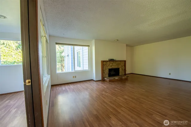 an empty room with wooden floor fireplace and windows