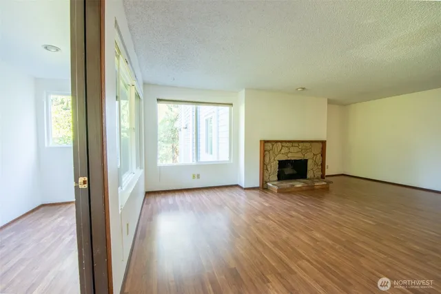 an empty room with wooden floor fireplace and windows