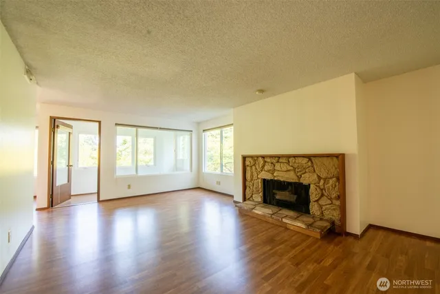 an empty room with wooden floor fireplace and windows