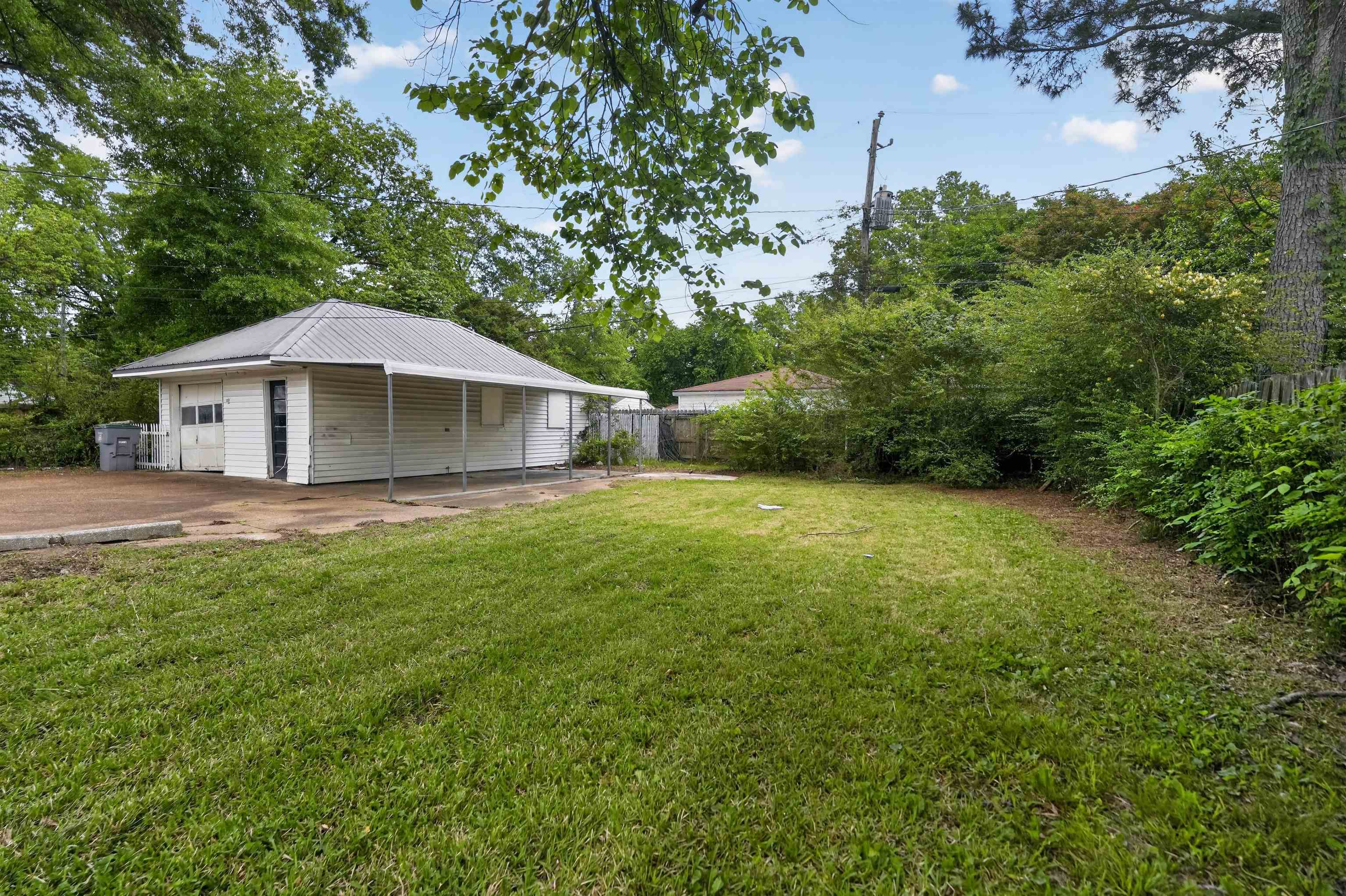 Expansive grassy yard area alongside a detached structure featuring a metal roof, white siding, and a covered patio area